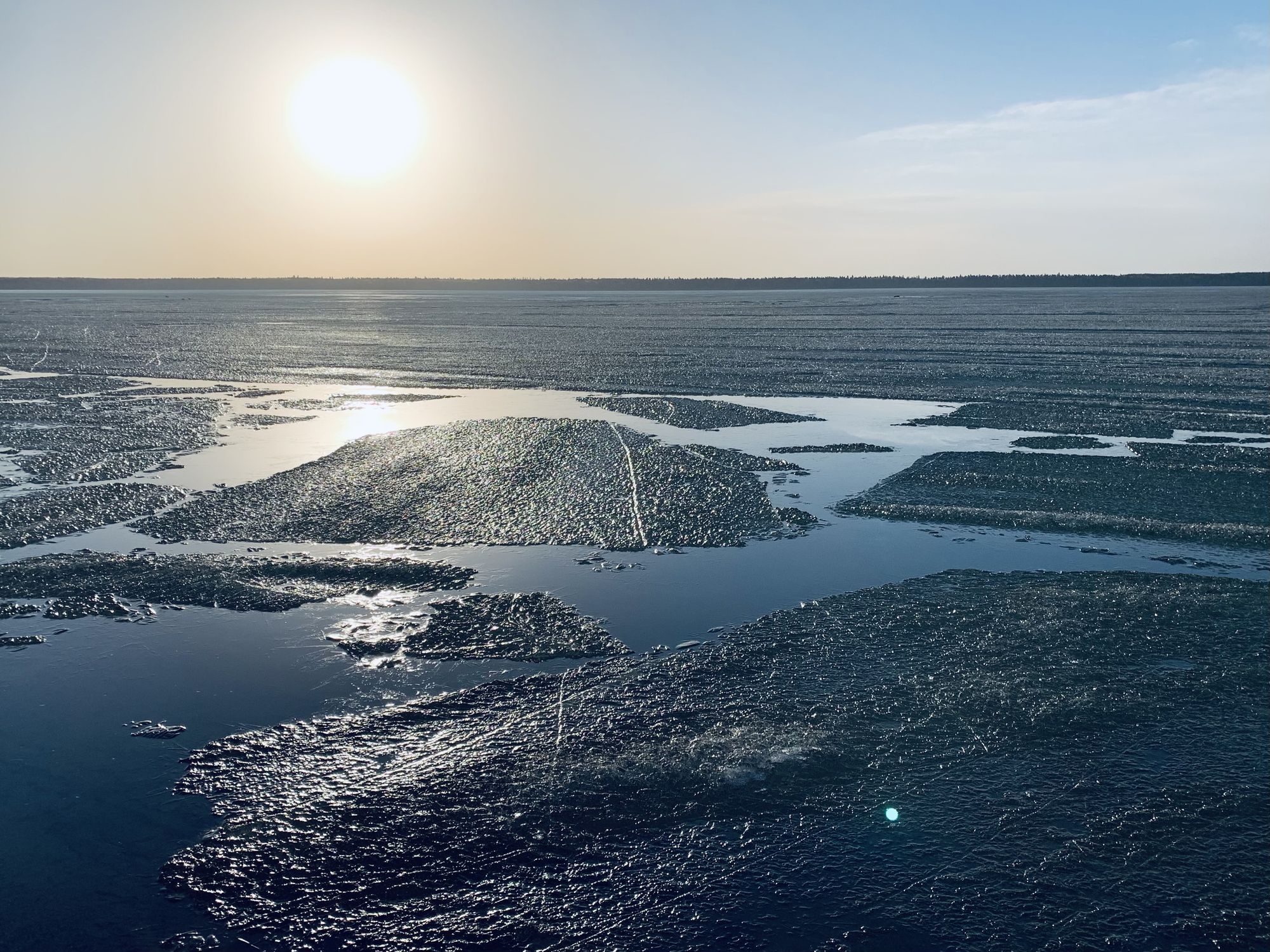 Ice melting on a lake. The sun rises over the horizon in the background.